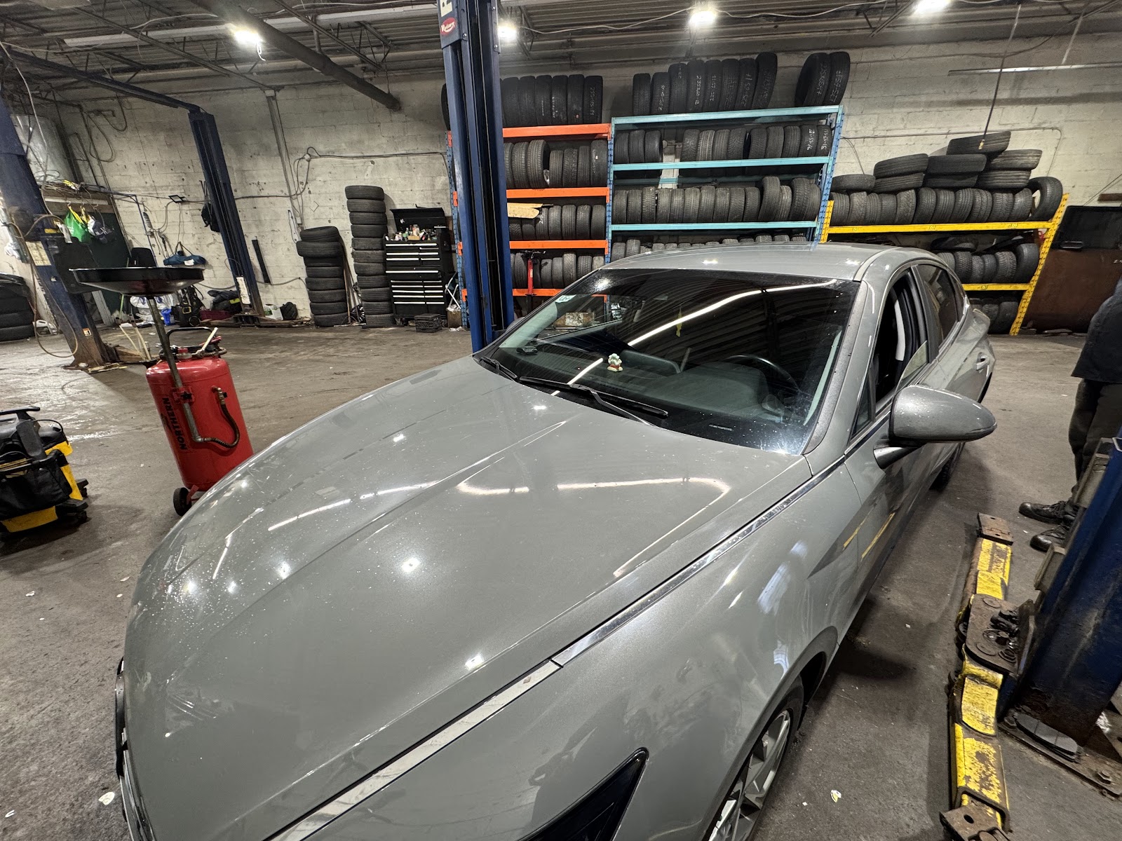 Car on the lift inside the Khan Autos workshop with tire racks behind